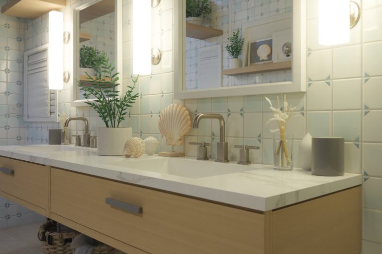 Modern bathroom with dual sinks, light wood vanity, large mirrors, wall sconces, and seashell decor. Green plants and storage baskets add a fresh, coastal touch. Blue and white geometric tile backsplash.